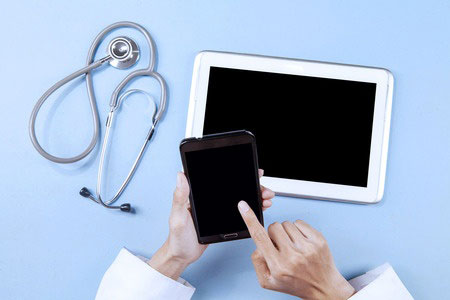 doctor handles smartphone with tablet and stethoscope on the table below