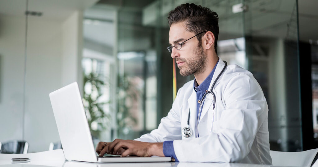 A healthcare provider sits at a laptop writing detailed SOAP notes to document patient interactions.