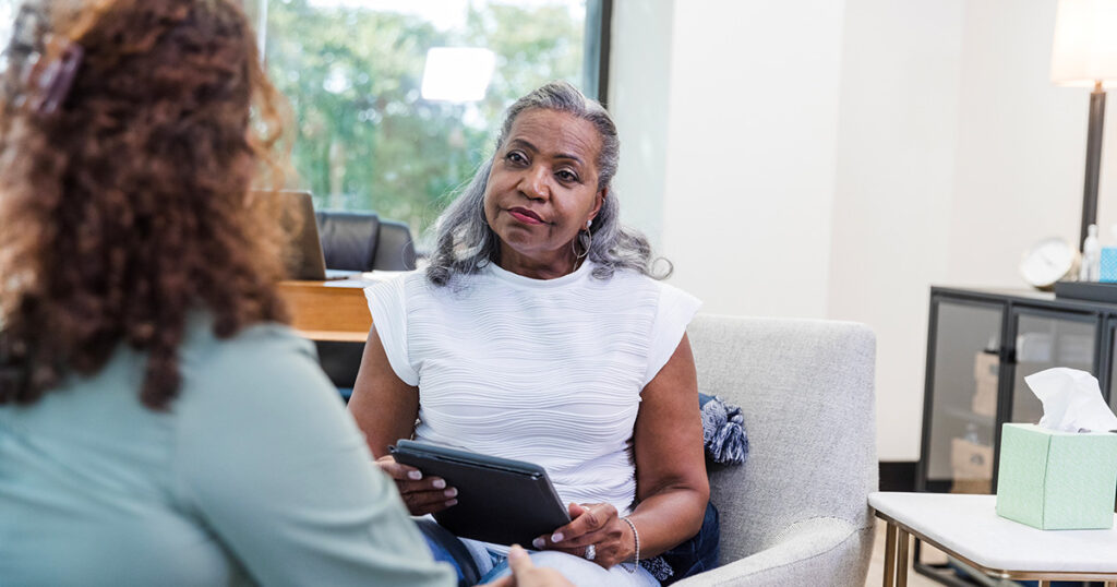 A therapist listens to her client while taking notes on a clipboard for effective therapy documentation.